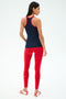 A woman faces away, wearing the SPLITS59 Ashby Rib Tank in Indigo/Pirate Red—ideal gym attire—paired with red leggings and white athletic shoes with red stripes against a plain light background.