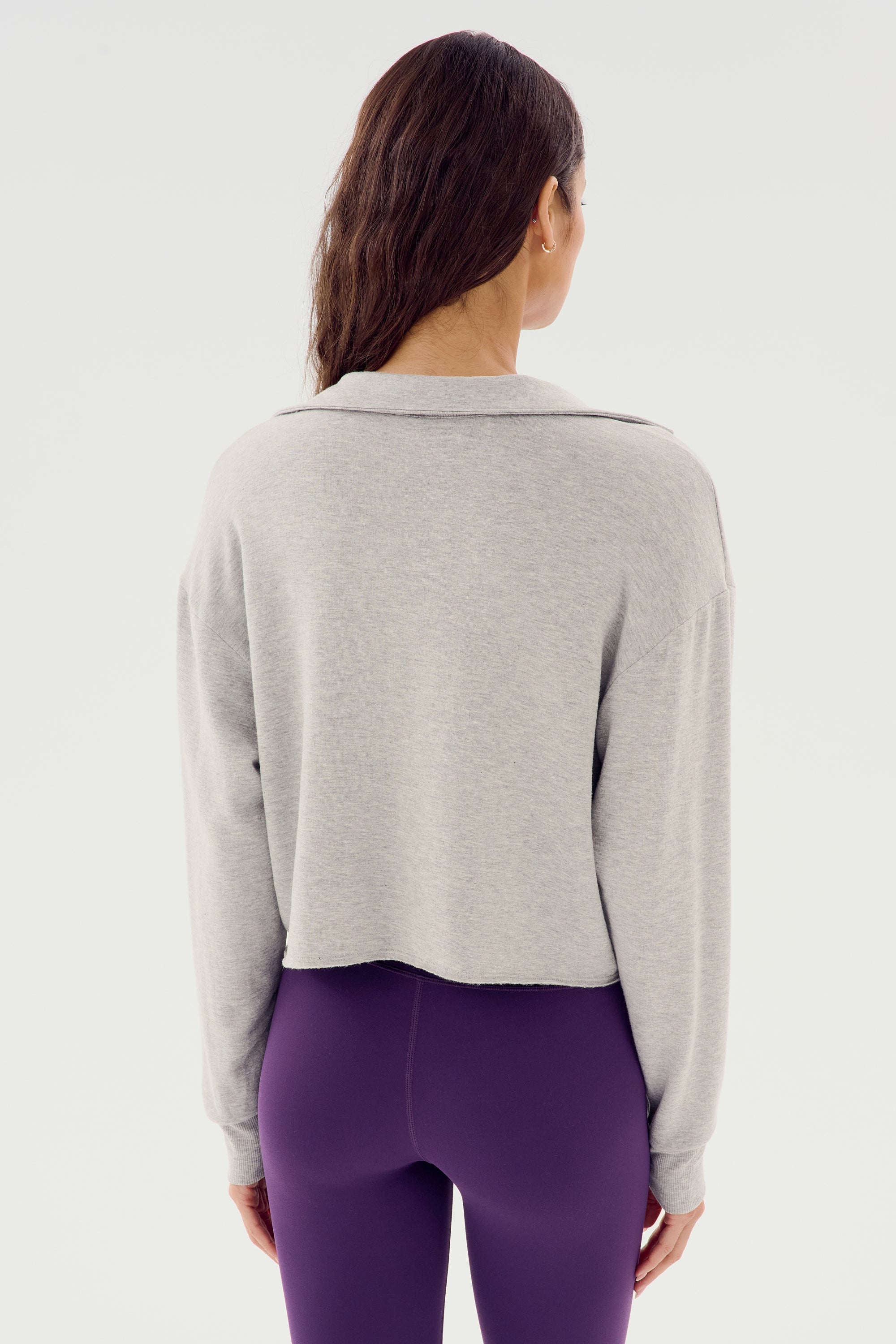 A person with long hair, seen from the back, wearing the SPLITS59 Joan Fleece Polo Sweatshirt in Heather Grey and purple high-waisted spandex leggings.