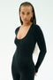A woman with long braided hair wears the SPLITS59 Chloe Airweight Jumpsuit in black and gold hoop earrings, standing against a plain light background.