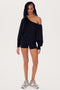 A woman wearing a black SPLITS59 Indy Dolman Fleece Sweatshirt, black shorts, and sneakers stands facing the camera.