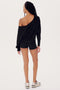 A woman standing with her back to the camera, wearing a black off-the-shoulder SPLITS59 Indy Dolman Fleece Sweatshirt, shorts, and sneakers, on a white background.