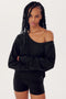 A woman with braided hair wearing a black SPLITS59 Indy Dolman Fleece Sweatshirt and shorts, standing with her arms crossed.