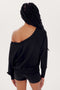 A woman with braided hair sporting a black off-the-shoulder SPLITS59 Indy Dolman Fleece Sweatshirt and shorts, viewed from the back against a white background.