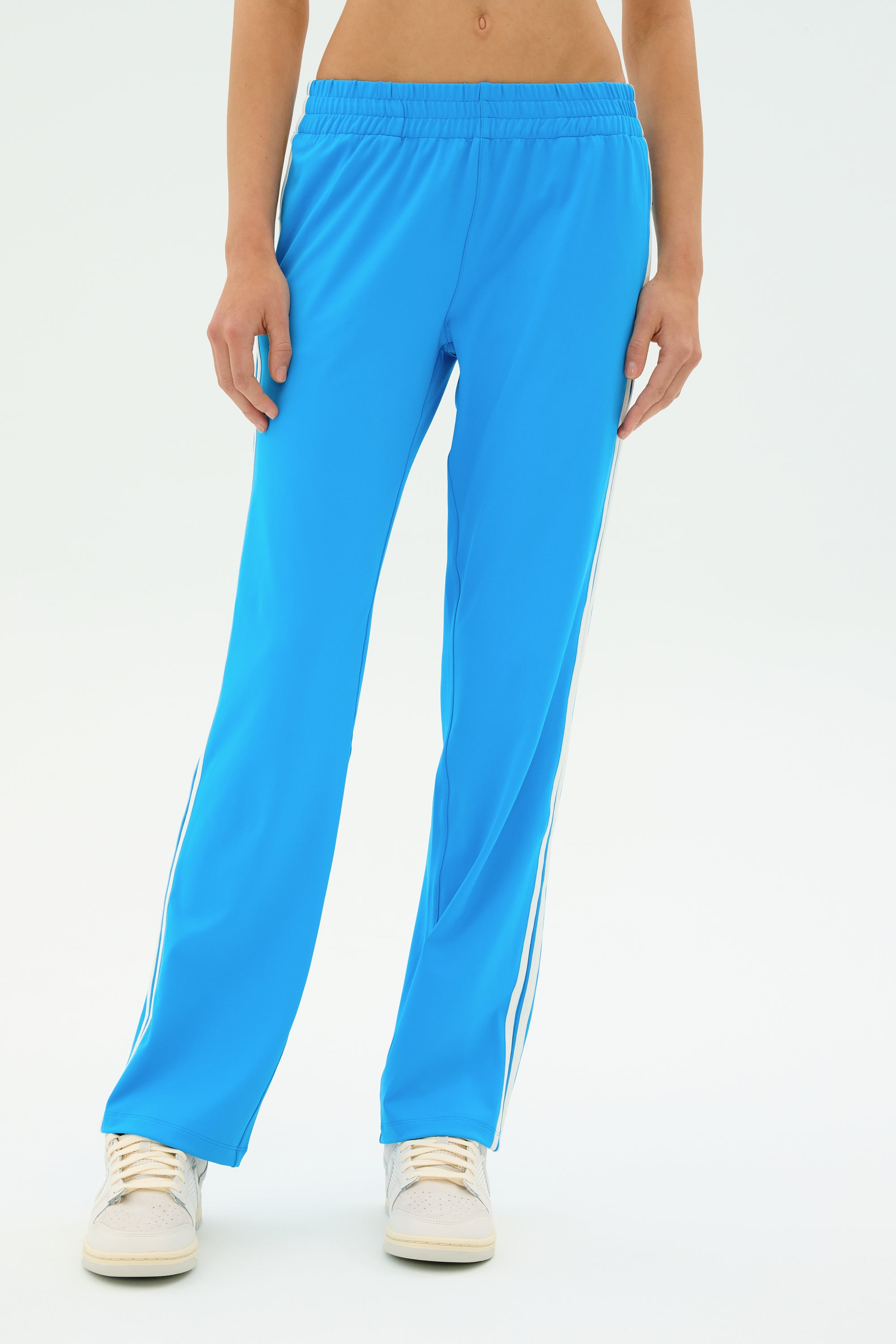 Model wears the SPLITS59 Fox Recycled Techflex Pant in Riviera/White with white sneakers, highlighting a sporty style against a plain white backdrop.