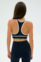 A person wearing the SPLITS59 Layla Airweight Bra in Indigo/White and matching leggings, with long hair down, stands against a plain white background.