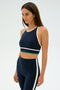 A woman in a SPLITS59 Layla Airweight Bra, featuring an indigo and white design, stands against a plain background.