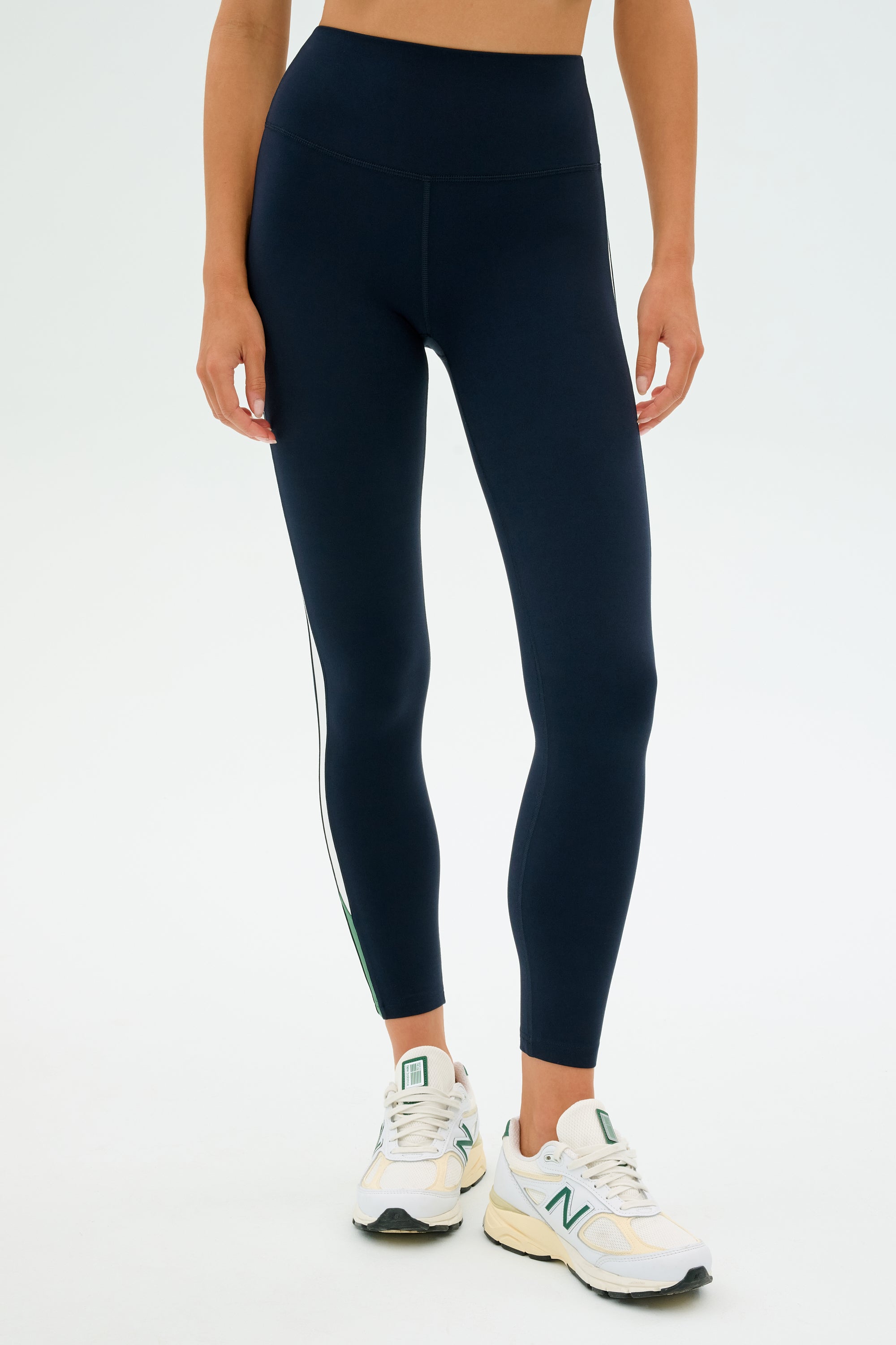 Someone wearing SPLITS59's Layla Airweight High Waist 7/8 leggings in Indigo/White and white sneakers stands against a plain background.