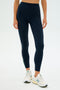 Someone wearing SPLITS59's Layla Airweight High Waist 7/8 leggings in Indigo/White and white sneakers stands against a plain background.