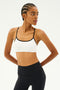Against a white backdrop, an individual wears the Loren Seamless Bra in White/Black by SPLITS59, paired with black leggings. Their arms are positioned behind their back, showcasing a readiness for gym workouts while enjoying chafe-free comfort.