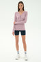 A woman stands against a plain background wearing the SPLITS59 Louise Rib Henley in blush, black biker shorts, white crew socks, and white sneakers.