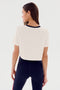 A person with long hair, wearing a SPLITS59 Djuna Crop Ringer - White/Indigo and black leggings with red stripes, is looking to the side, facing away from the camera against a plain background.