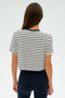 A long-haired fitness enthusiast wears SPLITS59's Djuna Crop Ringer in Indigo Stripe paired with black pants. With their back to the camera against a plain background, they exude a passion for gym workouts.