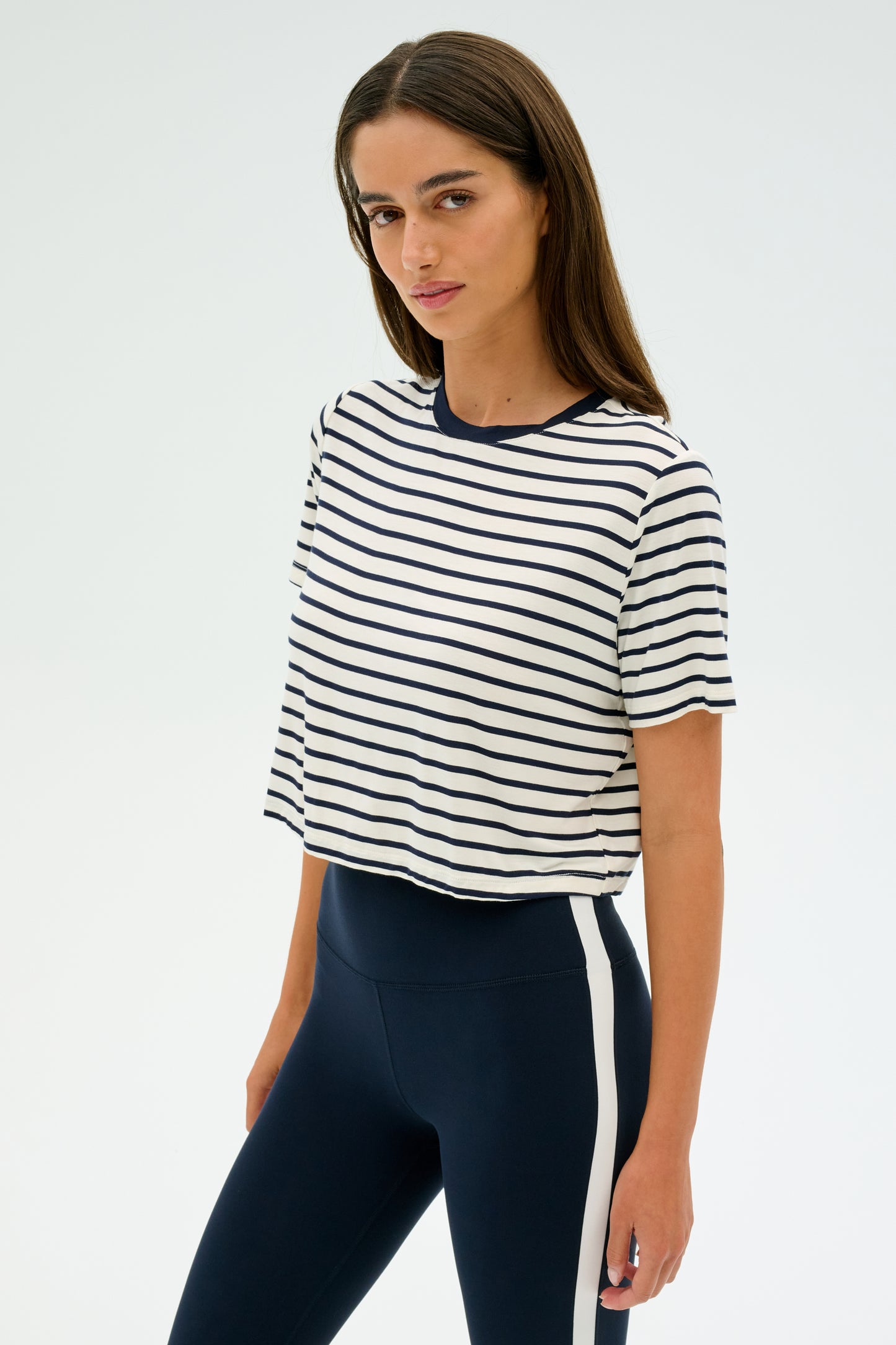 Wearing the Djuna Crop Ringer in Indigo Stripe from SPLITS59 and navy leggings with a white stripe, the individual stands against a plain background, symbolizing CrossFit's strength and focus.