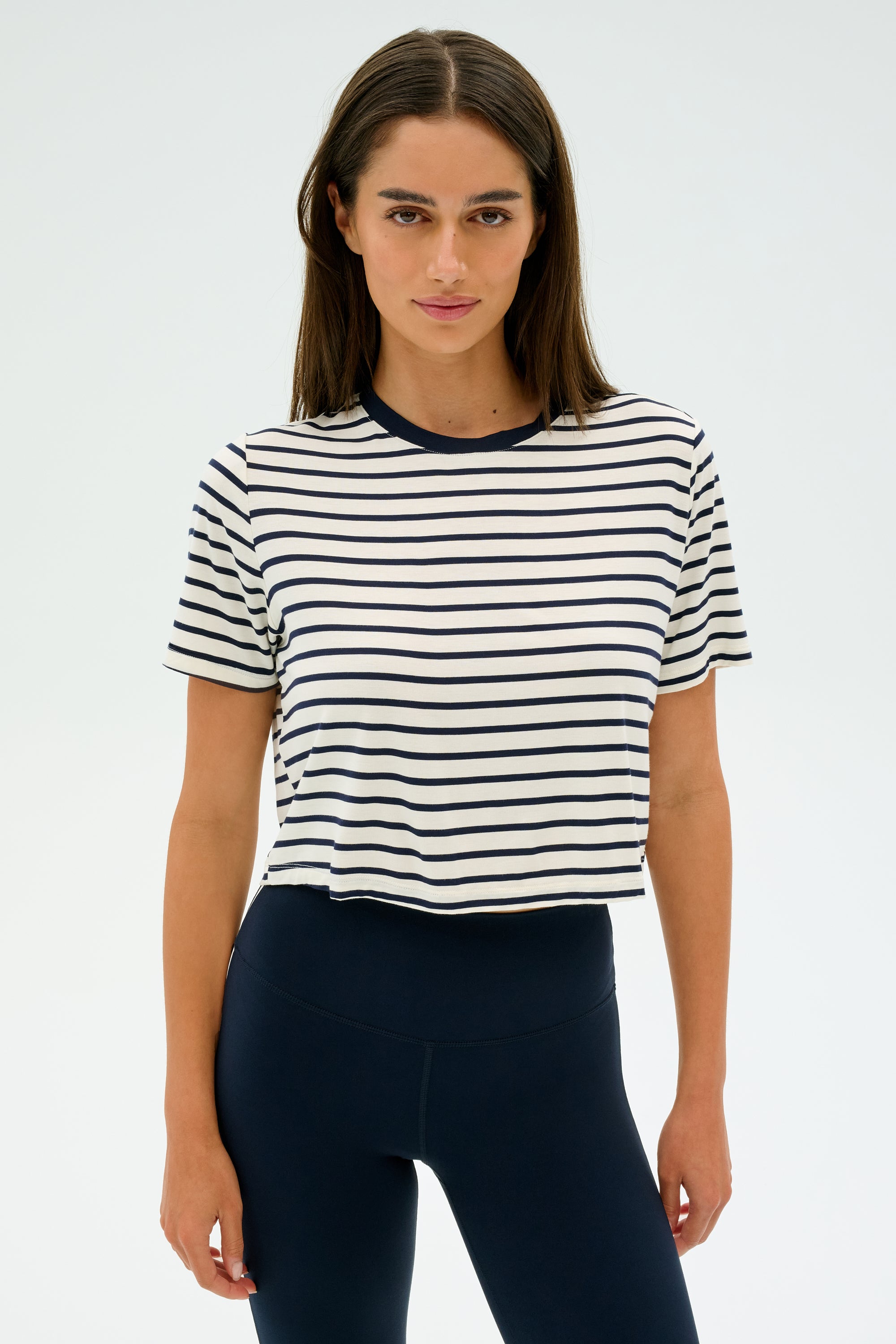 A person wearing the SPLITS59 Djuna Crop Ringer in Indigo Stripe and dark leggings stands against a plain background, ready for gym workouts.