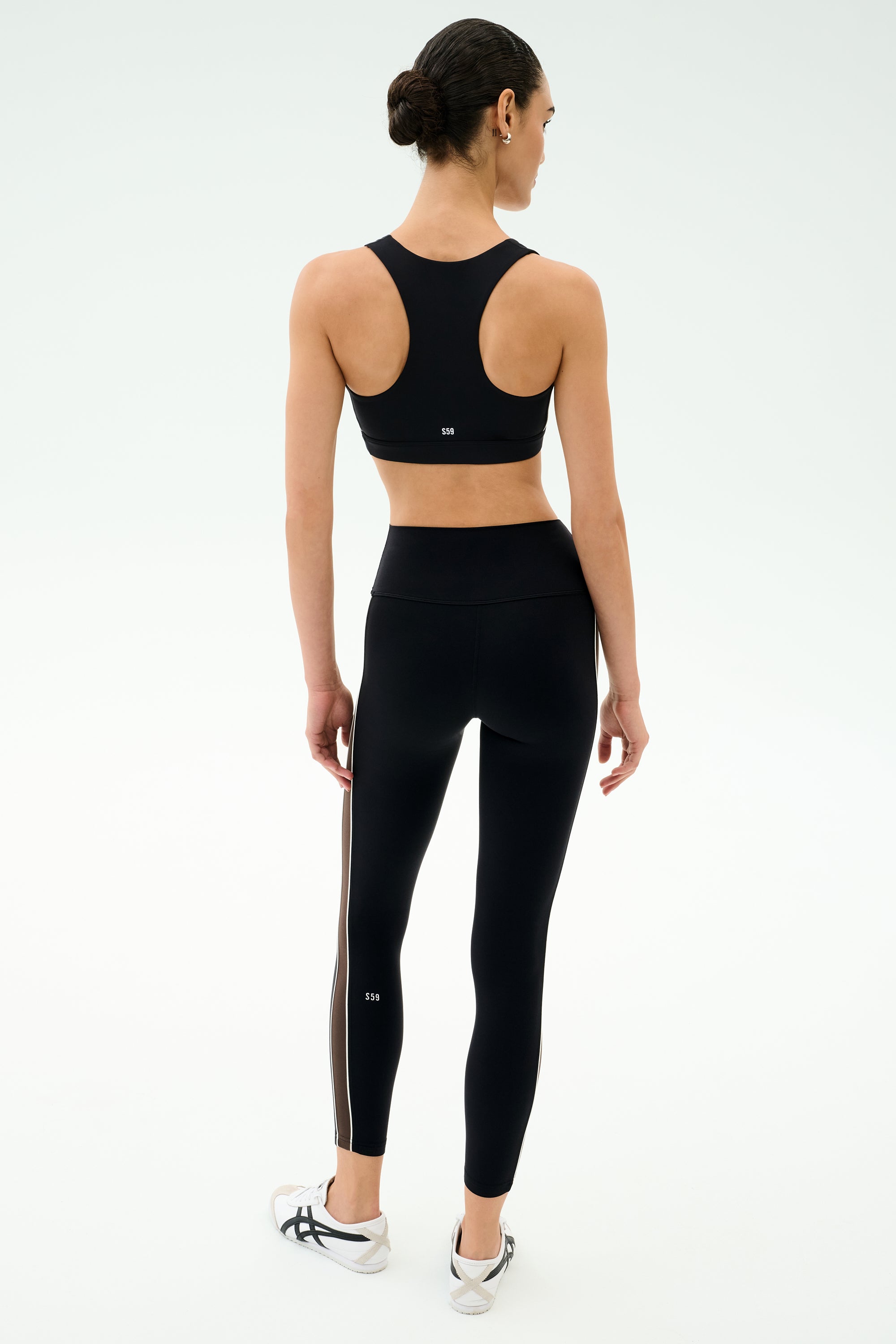 A woman wears the SPLITS59 Lexi Rigor Bra in Black/Dark Chocolate, standing with her back to the camera and arms by her sides against a plain light background.