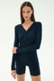 A woman stands against a plain background wearing the SPLITS59 Louise Rib Henley in Indigo with matching navy shorts.