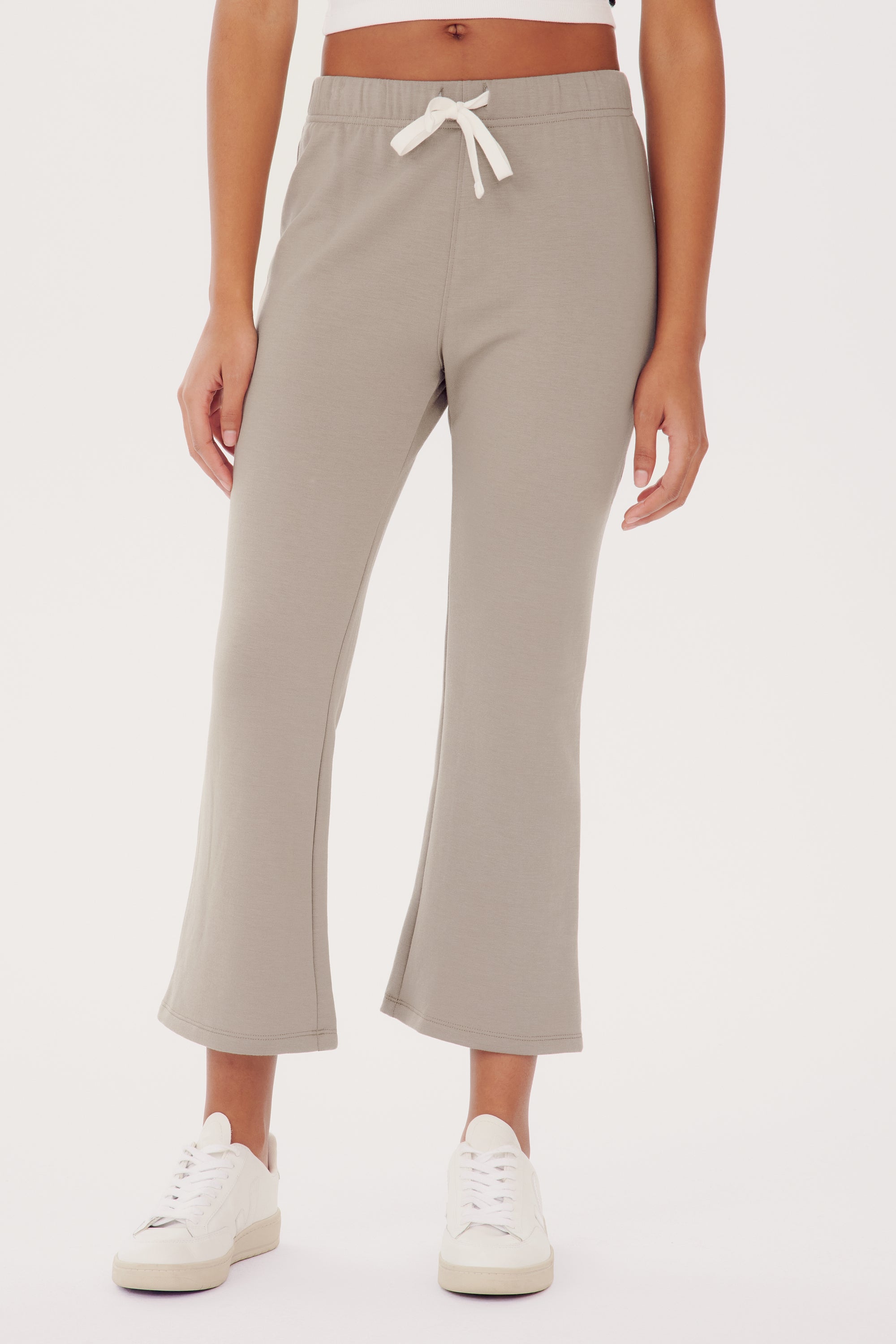 Woman wearing SPLITS59 Brooks Fleece Cropped Flare - Latte pants and white sneakers, standing against a plain background.