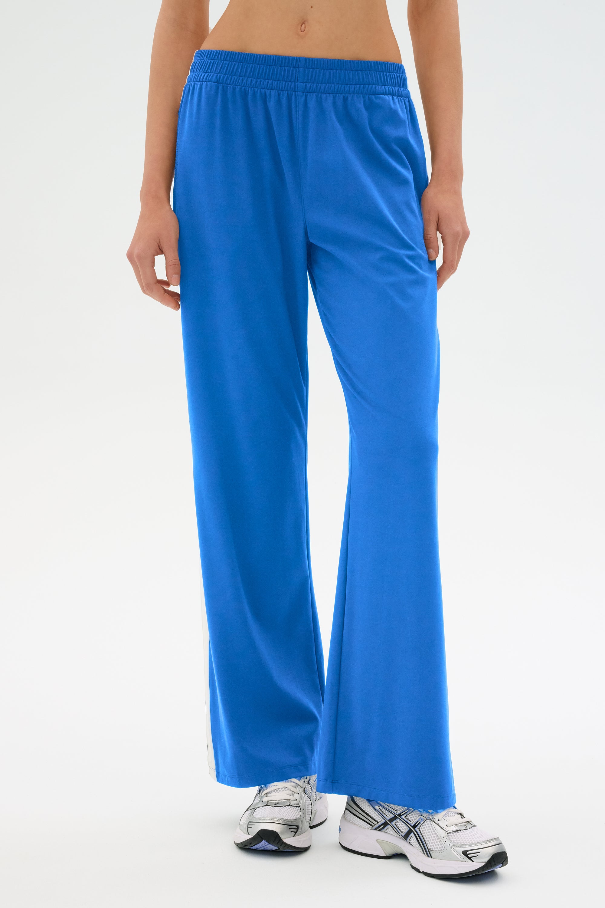 An individual is donning SPLITS59's Maxie Rigor Track Pant in bright blue alongside white sneakers against a plain background.