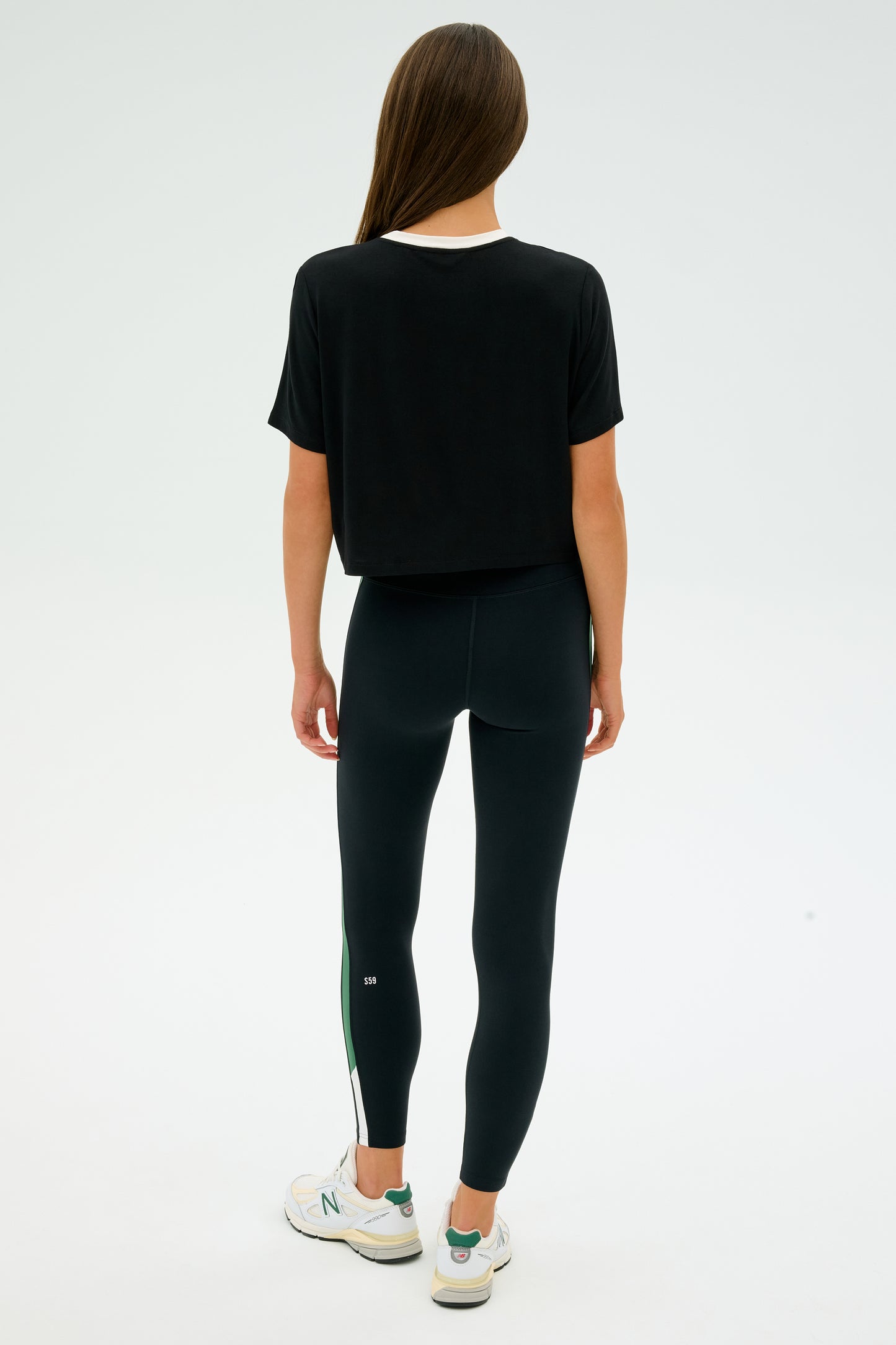 A person with long hair is seen from behind in the SPLITS59 Djuna Crop Ringer - Black/White, paired with leggings and stylish white and green sneakers, ready for CrossFit.