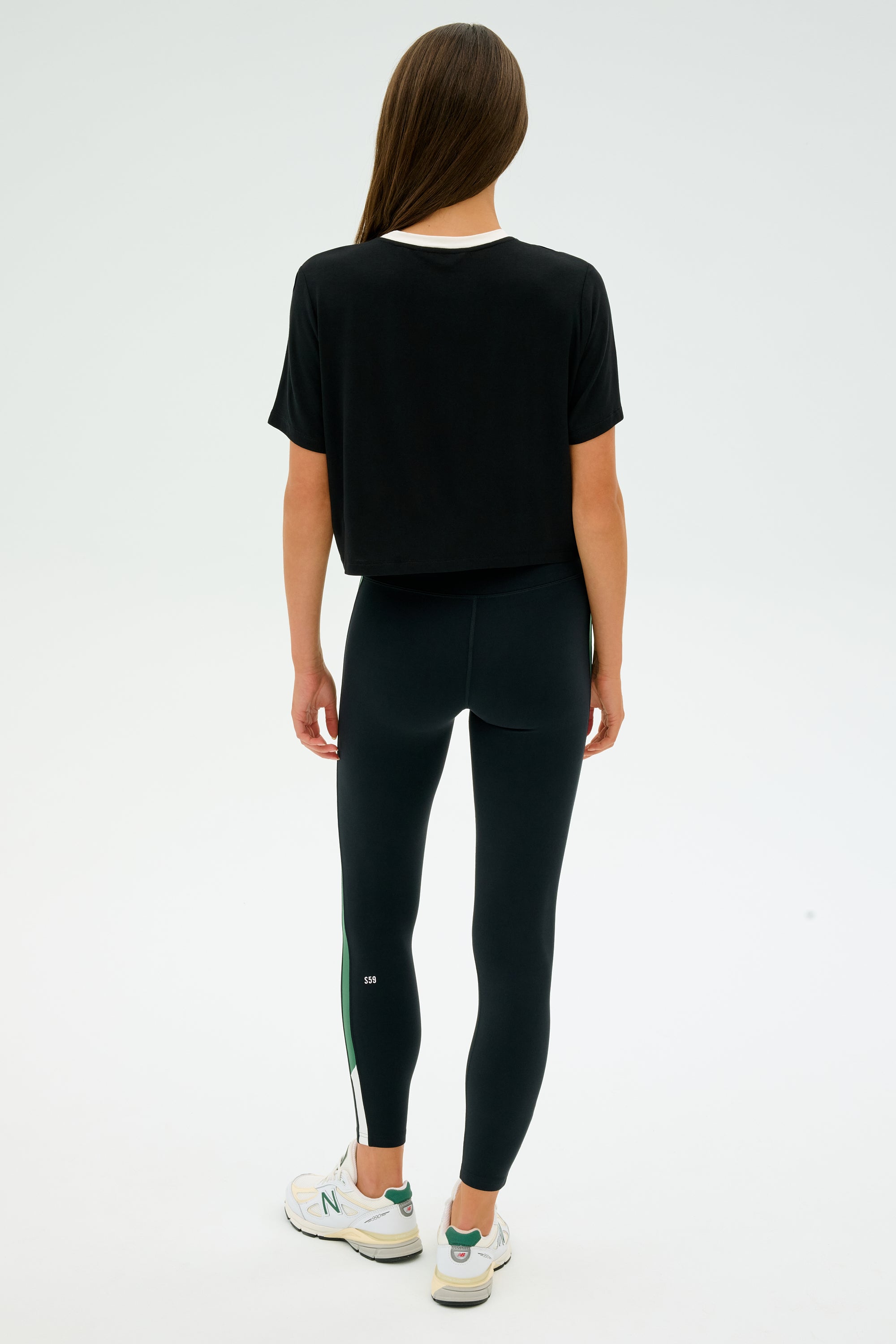 A person with long hair is seen from behind in the SPLITS59 Djuna Crop Ringer - Black/White, paired with leggings and stylish white and green sneakers, ready for CrossFit.