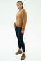 A person stands against a plain background wearing the SPLITS59 Joy Velour Crewneck in Honey, paired with black side-stripe leggings and brown athletic shoes.