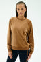 A woman with braided hair wears the SPLITS59 Joy Velour Crewneck in Honey, paired with dark side-striped stretch pants, standing against a plain light background.