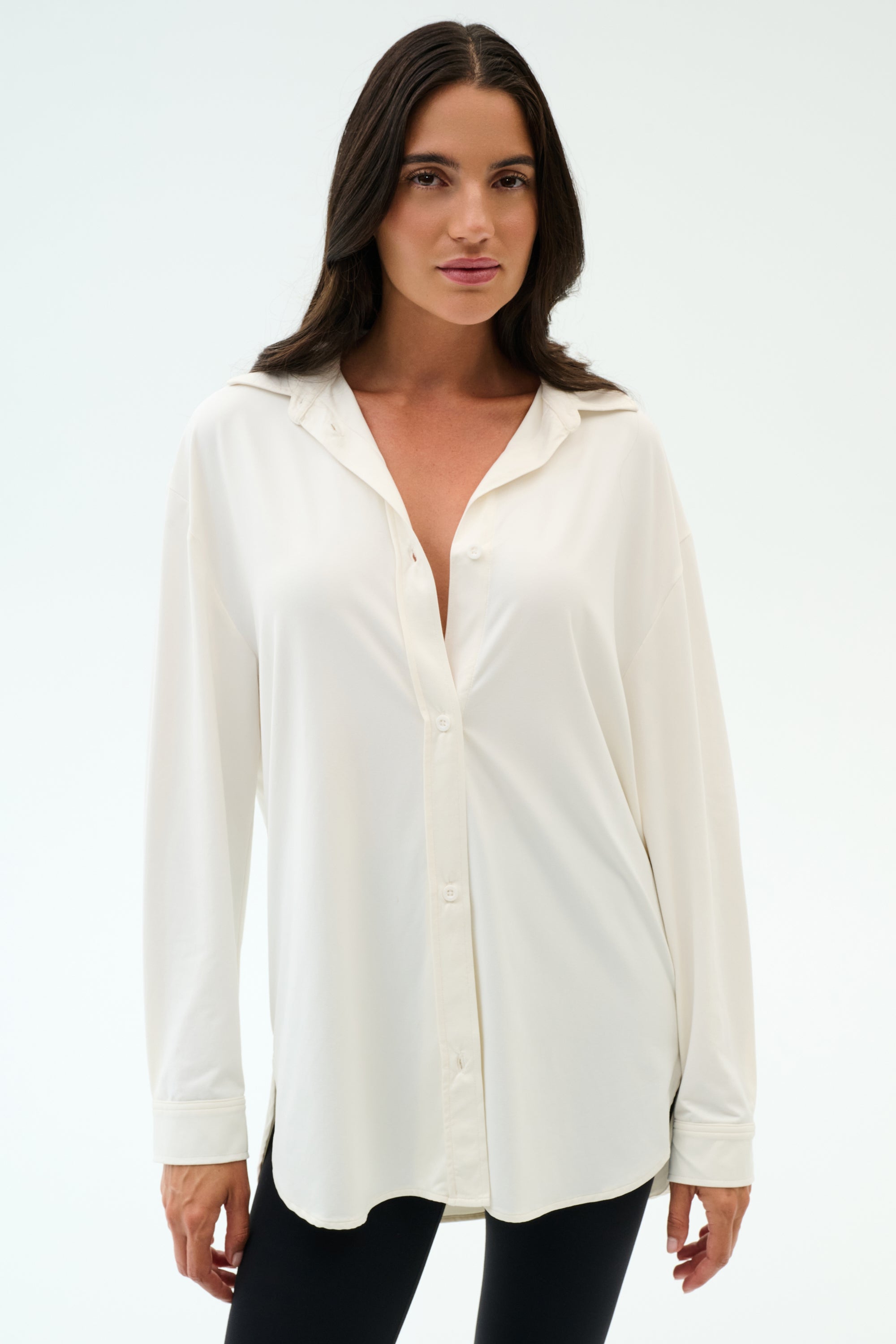 A woman with long brown hair models the SPLITS59 Kate Airweight Lite Button Down in white, paired with black pants, standing against a plain white background.