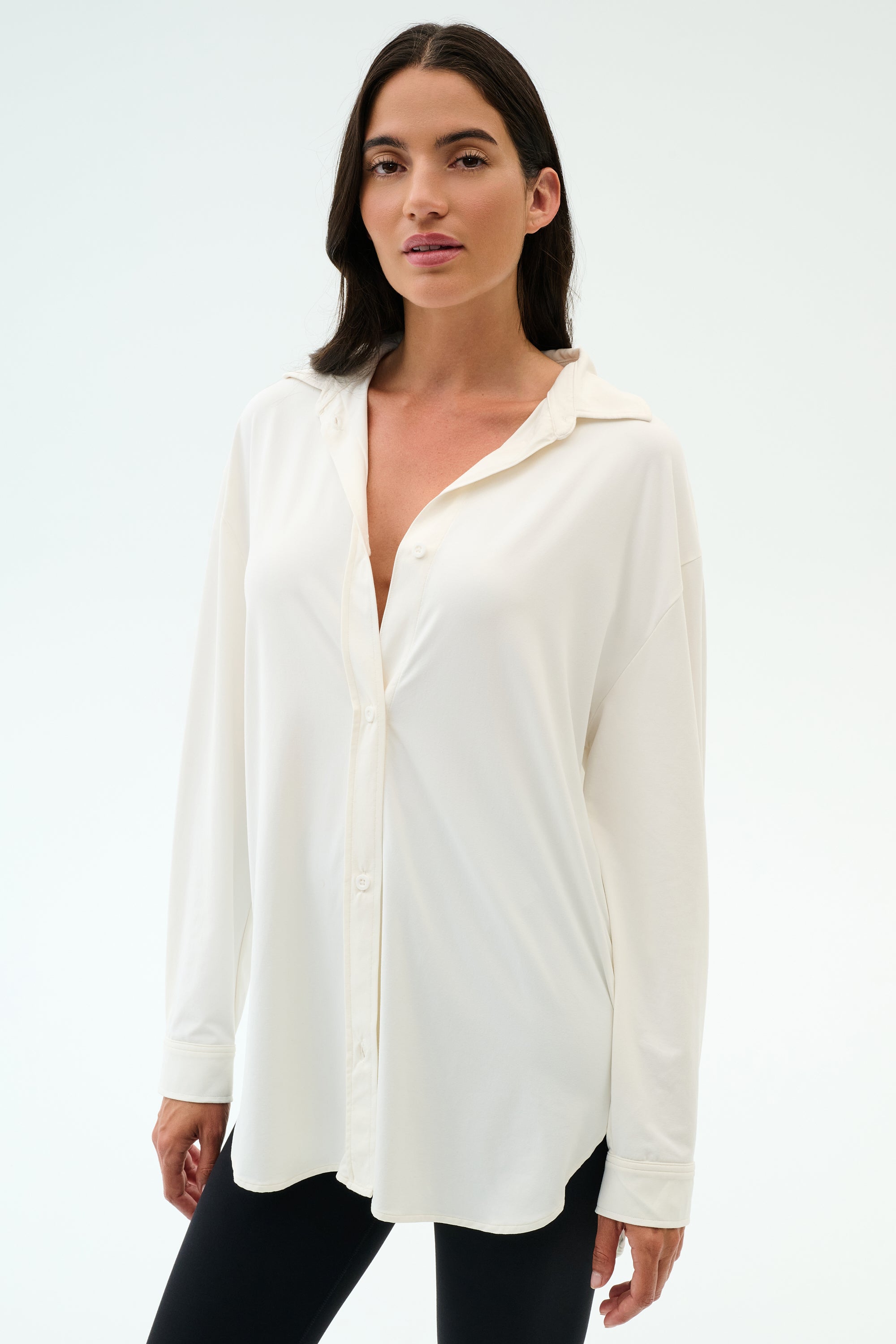 A woman wears the SPLITS59 Kate Airweight Lite Button Down in white with black pants against a light background—a versatile layering piece for any occasion.
