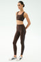 A woman stands against a plain background wearing the SPLITS59 Lexi Rigor Bra in Dark Chocolate/Black, paired with matching high-waisted leggings with white side stripes and white athletic sneakers—ideal for gym workouts.