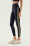 A person wearing the SPLITS59 Margot Rigor Legging in Black/Olive, white athletic shoes, and a black sports bra stands against a plain background.