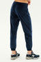 A person wearing SPLITS59's Rhys Velour Jogger in Indigo and grey New Balance sneakers, standing against a plain white background. The photo is taken from the back, focusing on the legs and footwear, epitomizing casual wear and comfort.