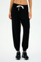 A person donning the SPLITS59 Andie Oversized Fleece Sweatpant in Black, paired with black sneakers and a white crop top, stands against a plain white background. Ideal for cool weather workouts and proudly MADE IN LOS ANGELES.