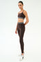 A person wears the SPLITS59 Cali Active Rib Bra in Heather Dark Chocolate, paired with matching leggings and white sneakers, standing against a plain white background.