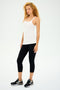 A person with curly hair stands stylishly against a plain background, wearing the white Charlie Rib Tank by SPLITS59, black leggings, and sleek black sneakers, ready for intense gym workouts.