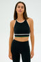 A person wearing the SPLITS59 Layla Airweight Bra in Black/Arugula stands against a plain background, fully dressed in an athletic ensemble.