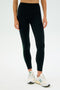 A person wearing SPLITS59 Layla Airweight High Waist 7/8 leggings and white sneakers stands against a plain background.
