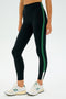A person wearing SPLITS59's Layla Airweight High Waist 7/8 in Black/Arugula, paired with white sneakers, stands against a plain background.