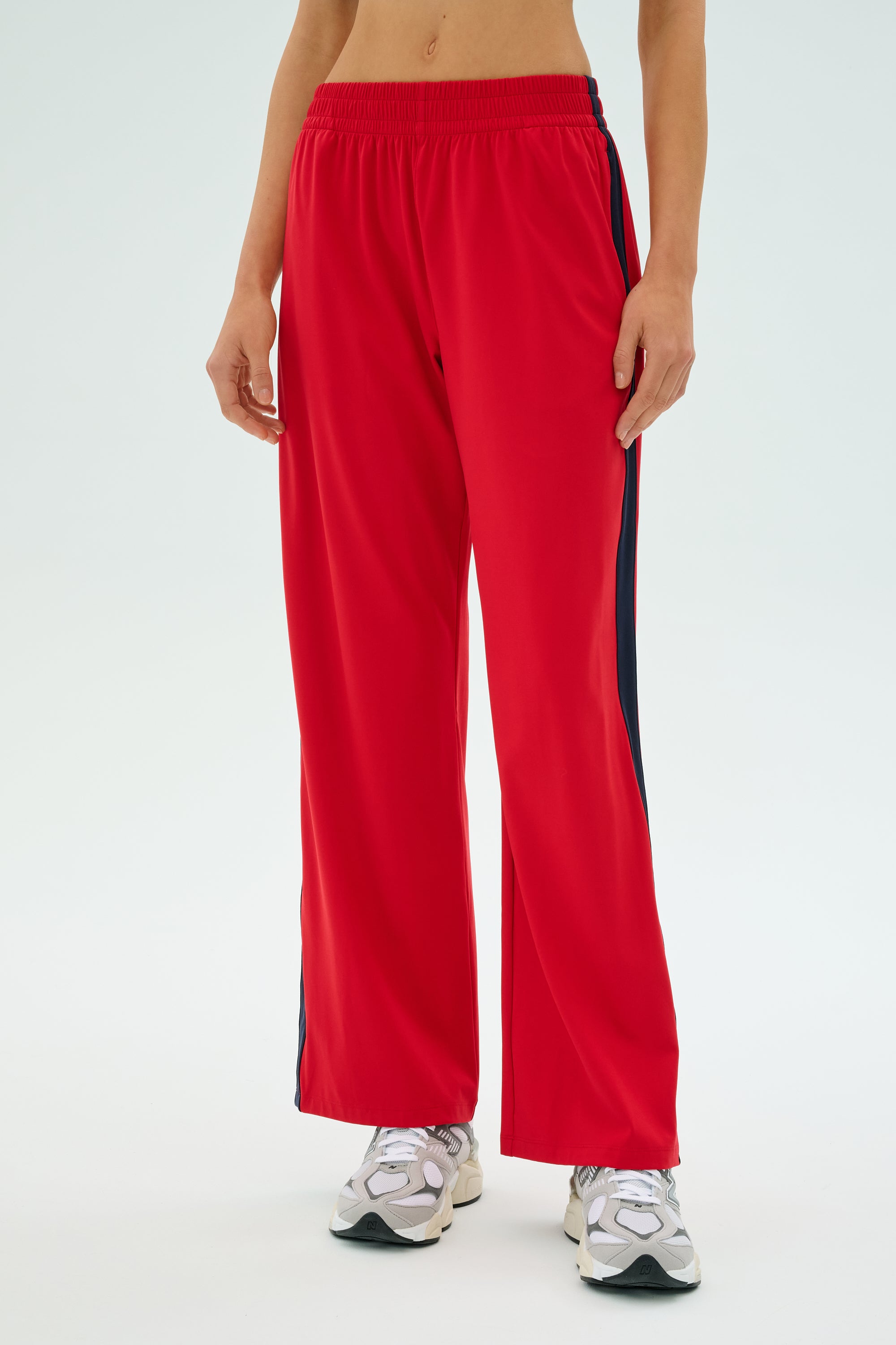 A person wearing SPLITS59's Maxie Rigor Track Pant in Pirate Red/Indigo with gray sneakers stands against a plain background.