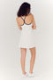 A woman with curly hair seen from behind, wearing a white SPLITS59 Simona Airweight Tank Dress and white sneakers.