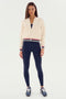 A woman stands against a plain background wearing the SPLITS59 Willa Sherpa Jacket in cream, featuring sporty striped cuffs and collar, paired with navy leggings and sneakers.