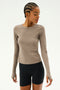 Dressed in a Lentil Airweight Lite Waist Length long-sleeve from SPLITS59 and black shorts, a person with braided hair stands against a neutral backdrop, ideal for enjoying the quick dry comfort during workouts.