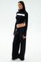 A woman stands against a plain background, wearing the SPLITS59 Brynn Airweight Pant in black, paired with a black and white long-sleeve spandex front-knot top and white sneakers.