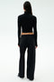 A person faces away, wearing SPLITS59's Brynn Airweight Pant in black, paired with a black spandex long-sleeve turtleneck and white sneakers against a plain light background.