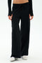 Wearing SPLITS59's Brynn Airweight Pant in Black with a black long-sleeve top and white sneakers, the person stands against a plain white background.
