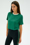 Dressed in the Djuna Crop Ringer t-shirt by SPLITS59, featuring arugula and white colors, paired with black leggings adorned with a green stripe, the person stands against a plain background.