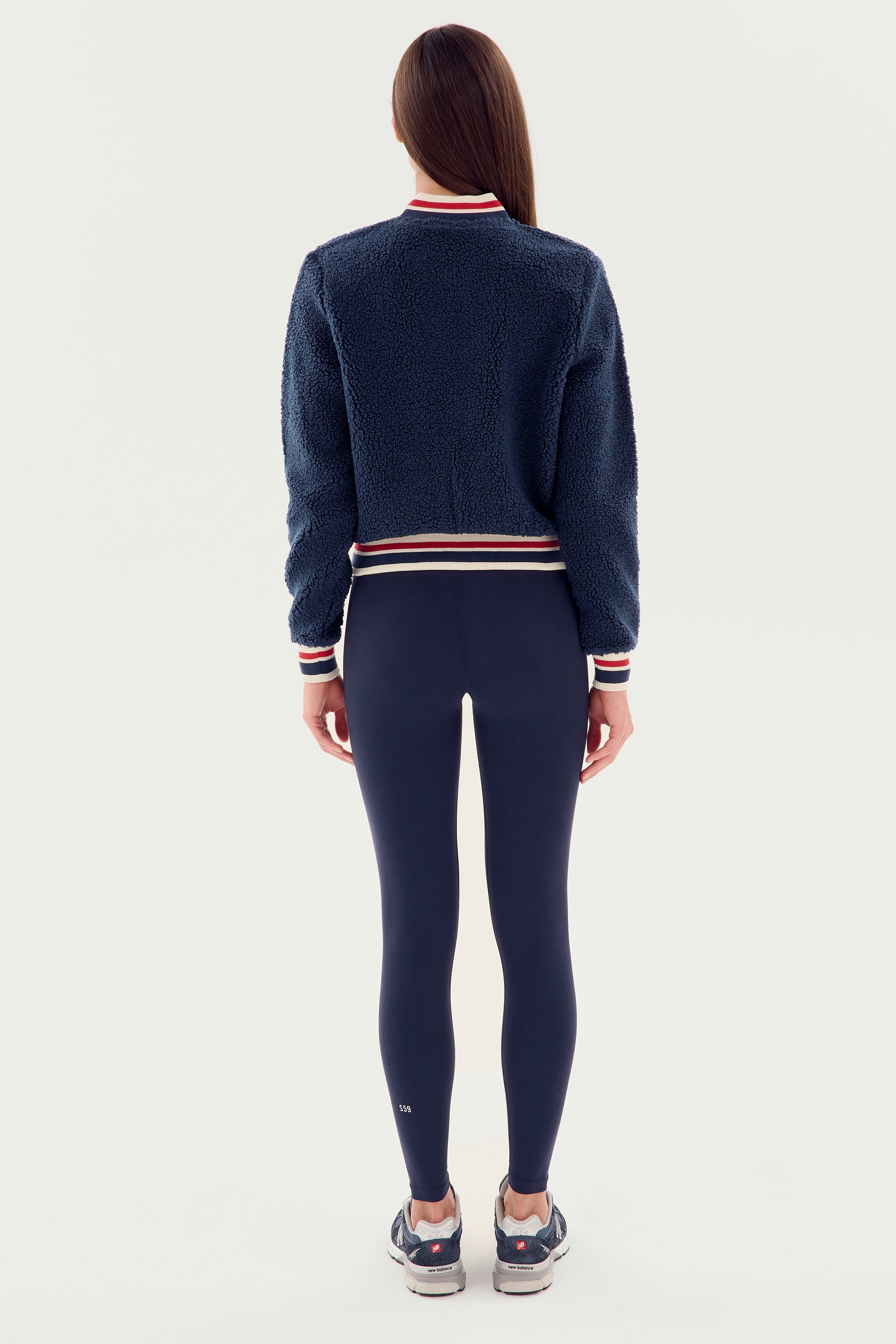 A person wearing the SPLITS59 Willa Sherpa Jacket - Indigo, black leggings, and black sneakers is shown from behind against a plain white background.