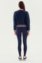 A person wearing the SPLITS59 Willa Sherpa Jacket - Indigo, black leggings, and black sneakers is shown from behind against a plain white background.
