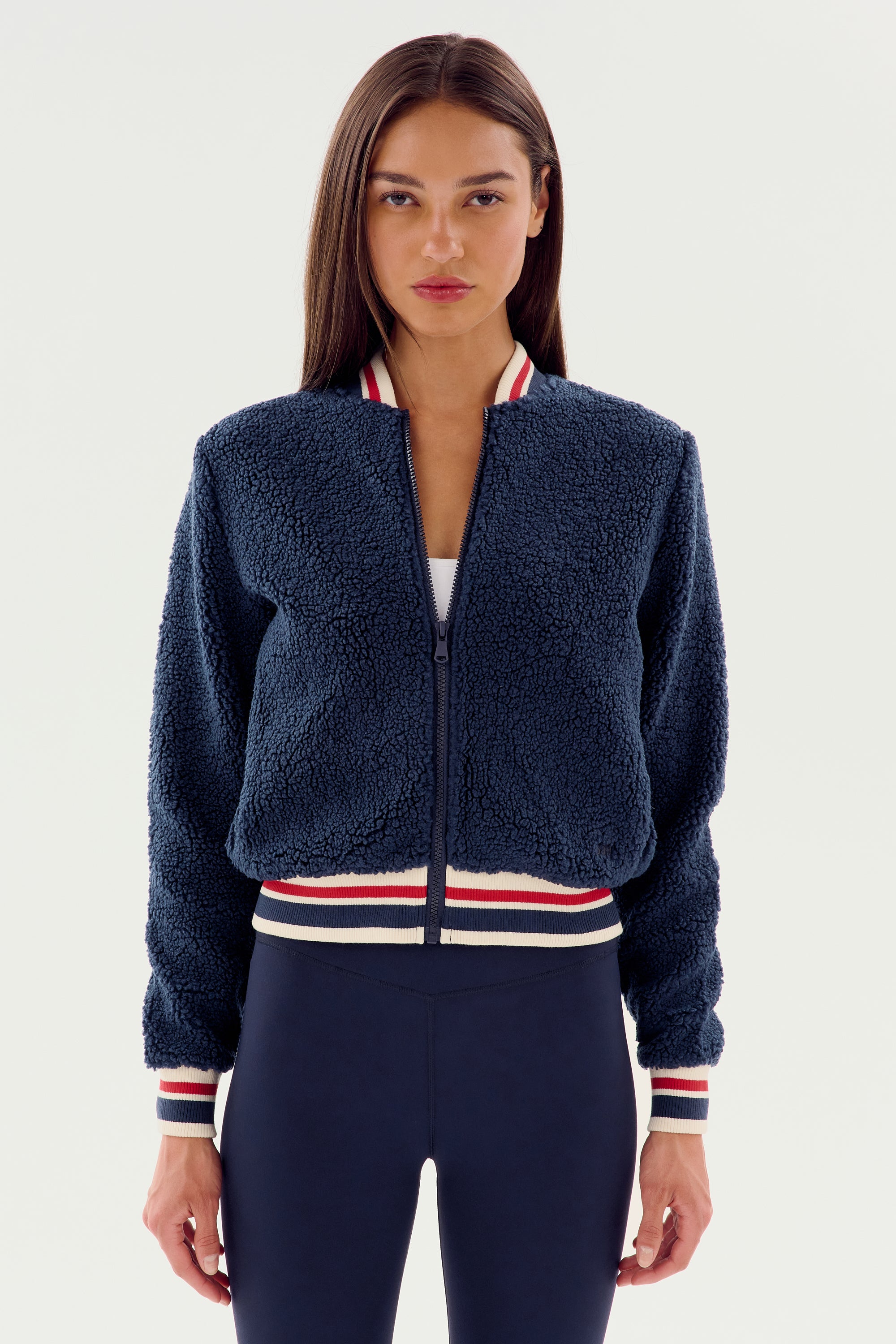 A person with long hair is wearing the Willa Sherpa Jacket - Indigo by SPLITS59, standing against a plain white background.