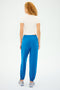 A woman with curly hair in a white short-sleeve top and SPLITS59 Andie Oversized Fleece Sweatpants in Classic Blue is ready for cool weather workouts.