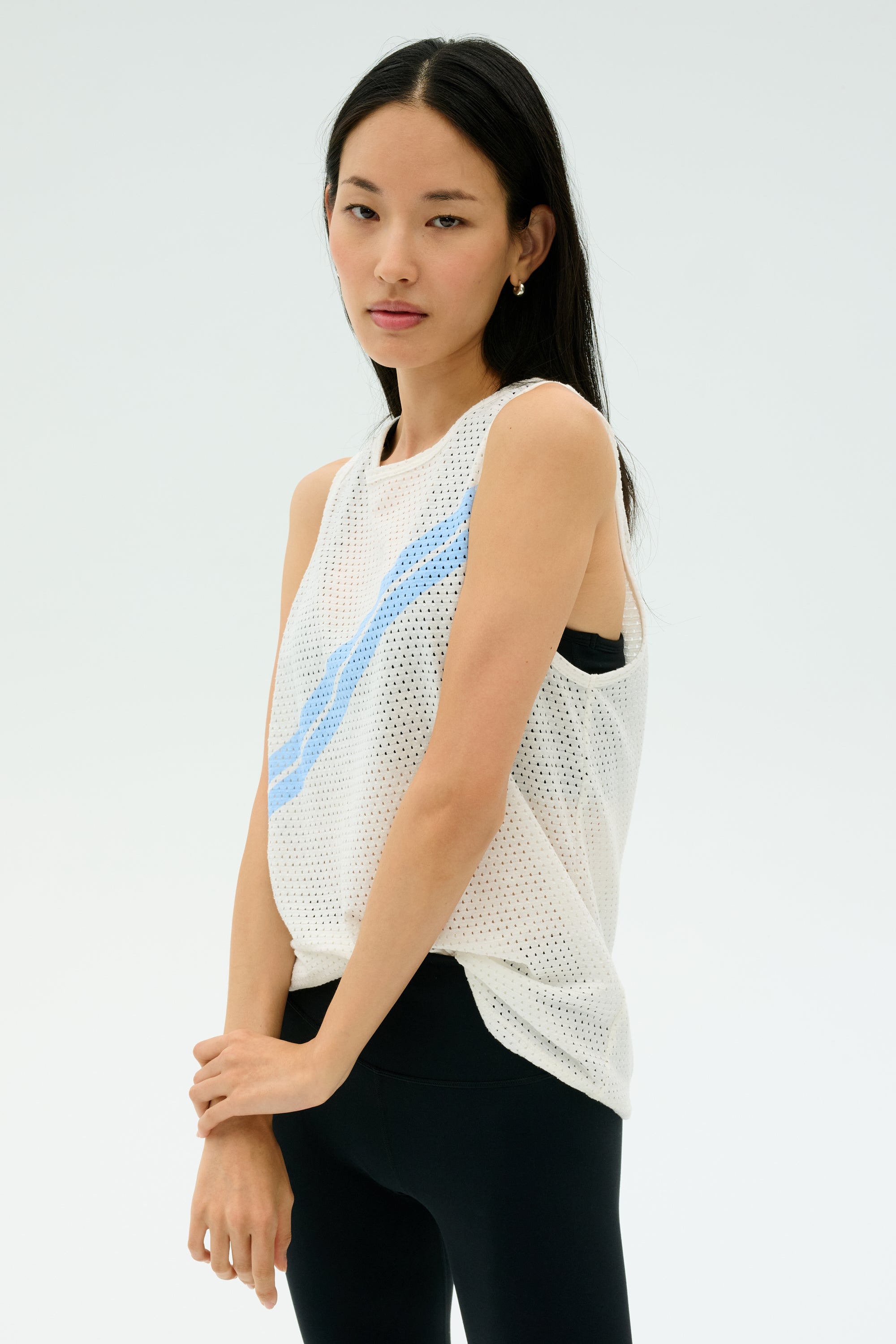 A woman with straight black hair wears the SPLITS59 Bandit Mesh Tank in White/Skylight over a black sports bra and leggings, standing against a plain light background.